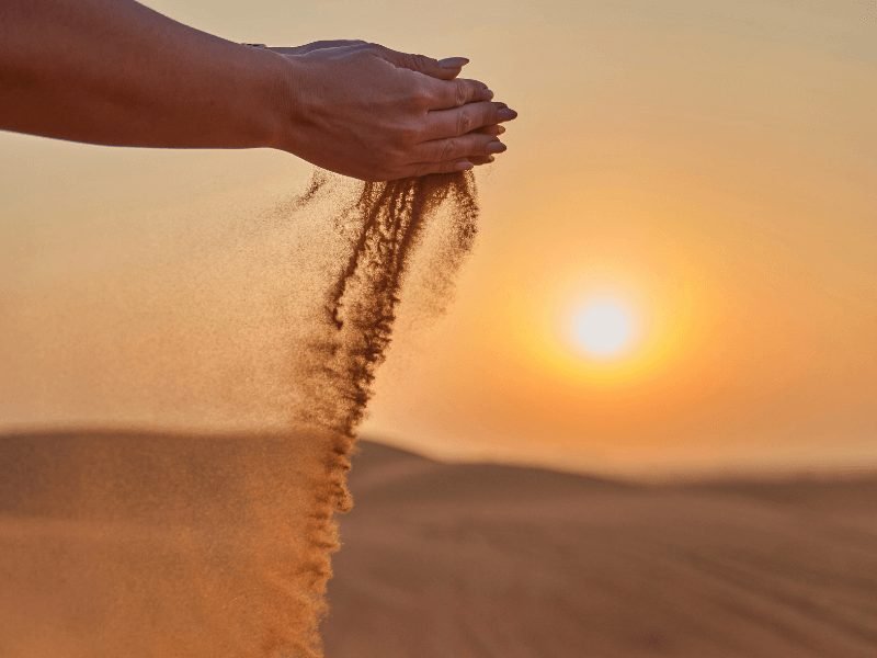 persons hands holding set and letting it drop through their fingers as the sun sets