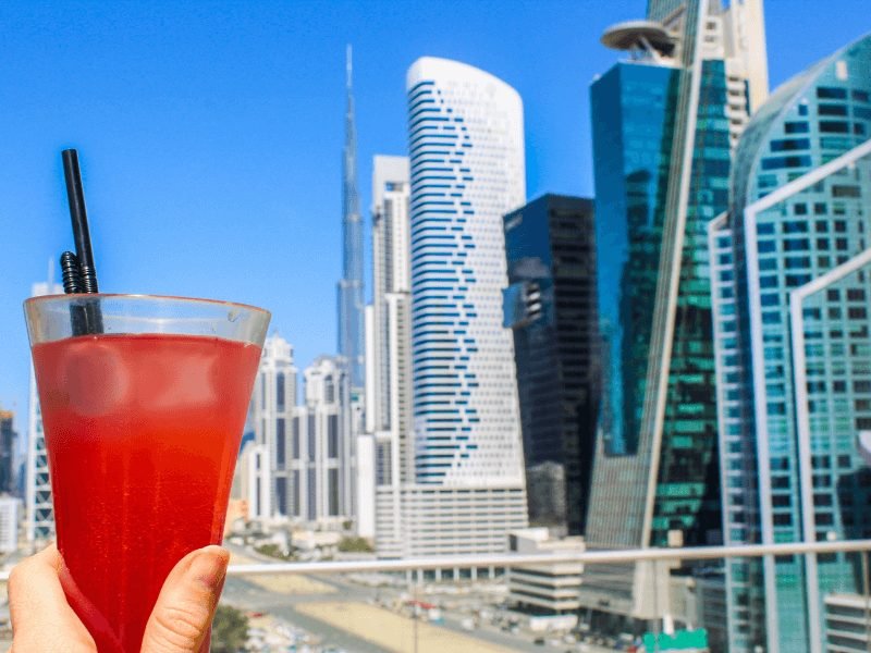 a traveler holding a drink with a straw in dubai with the skyline as the background