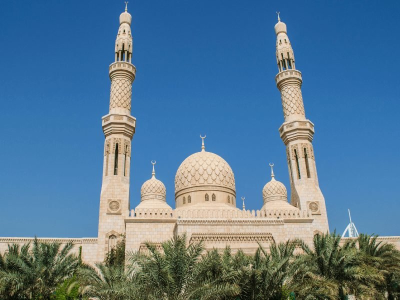 the jumeirah mosque with two minarets, palm trees in front, and domes: a must visit on your dubai itinerary