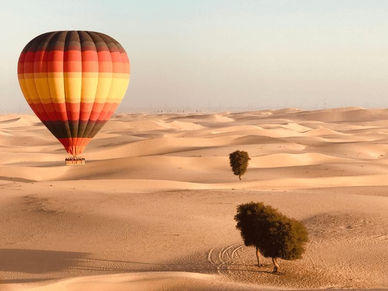 hot air balloon rising over the dubai desert with sand dunes and small trees