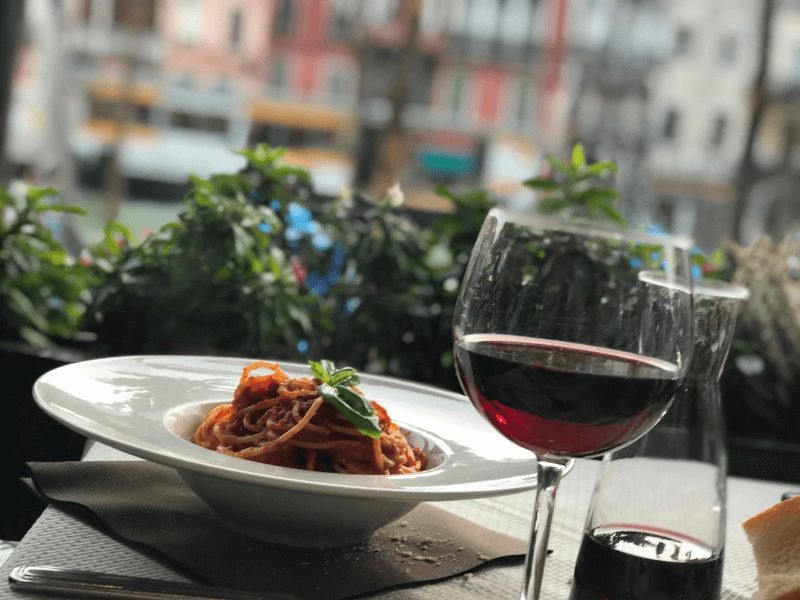 pasta with basil on top and a carafe of red wine with a blurred background of a european city