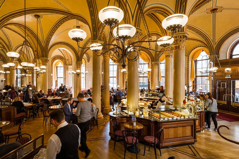 ornate interior of a vienna coffee house with arched ceiling, pretty tables, and lots of pastries