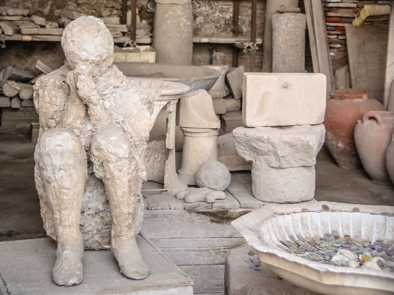 A seated plaster cast of a body in Pompeii, hands clasped together perhaps as in prayer