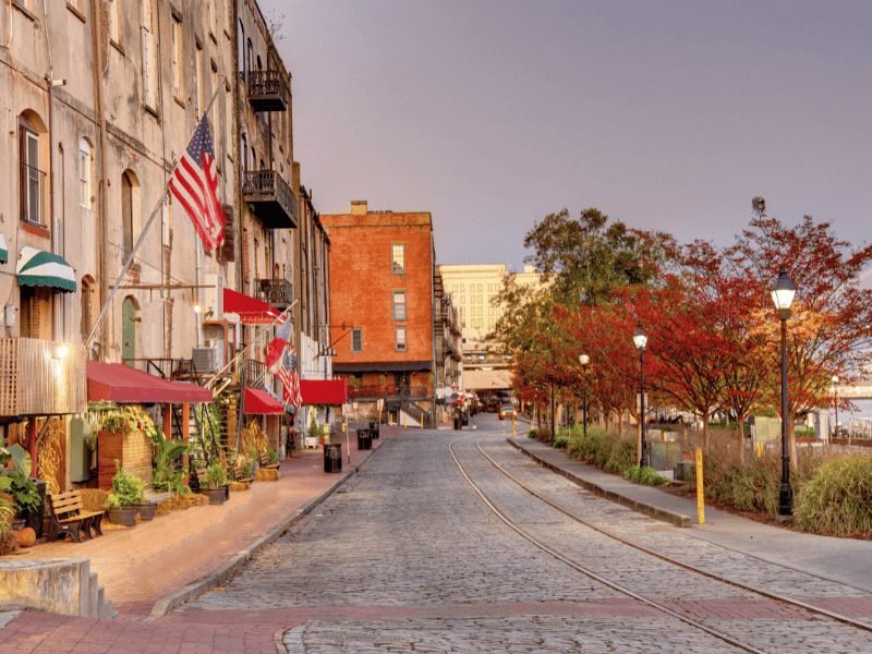 sunset scene at river street, with cobblestone, fall trees, american flags in savannah