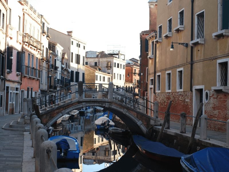 Bridge going over a canal in Venice with gondolas and walls of buildings on the side