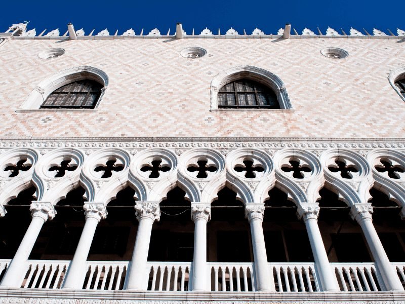 Looking up at the beautiful pillars and pink stone of Doge's Palace, a popular former palace in Venice that is now a museum.