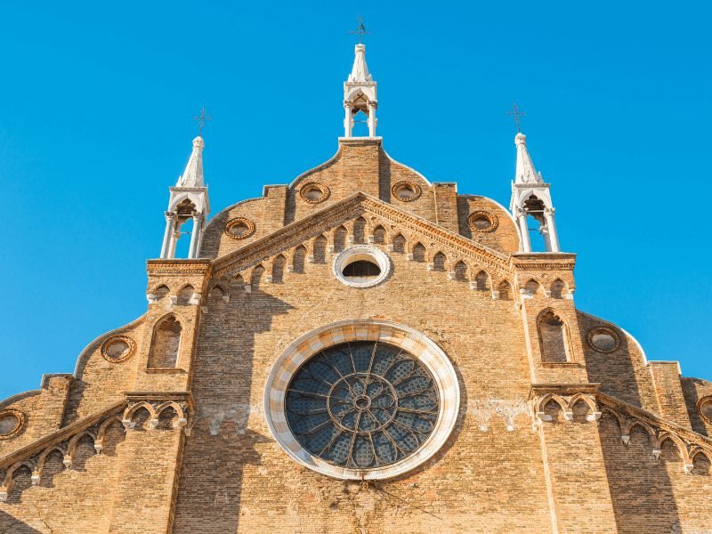 basilica in venice with brick facade and stained glass window and three white spires