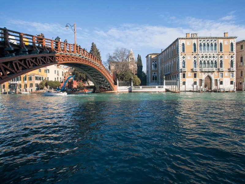wooden bridge in venice with the academia gallery behind it across the canal