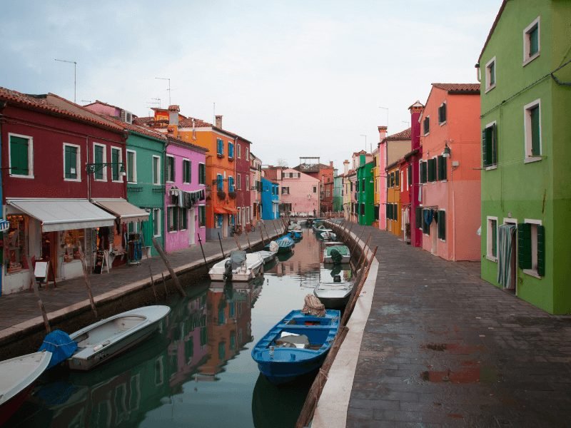 houses in all colors of the rainbow with small little boats on a canal in burano 