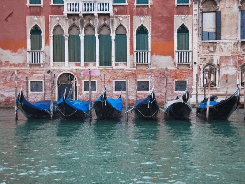 venice gondolas all lined up in a row next to an old-looking building facade on a canal