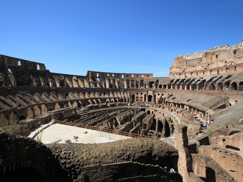 The Roman Colosseum from the interior with people walking around and view of the arena on a sunny day