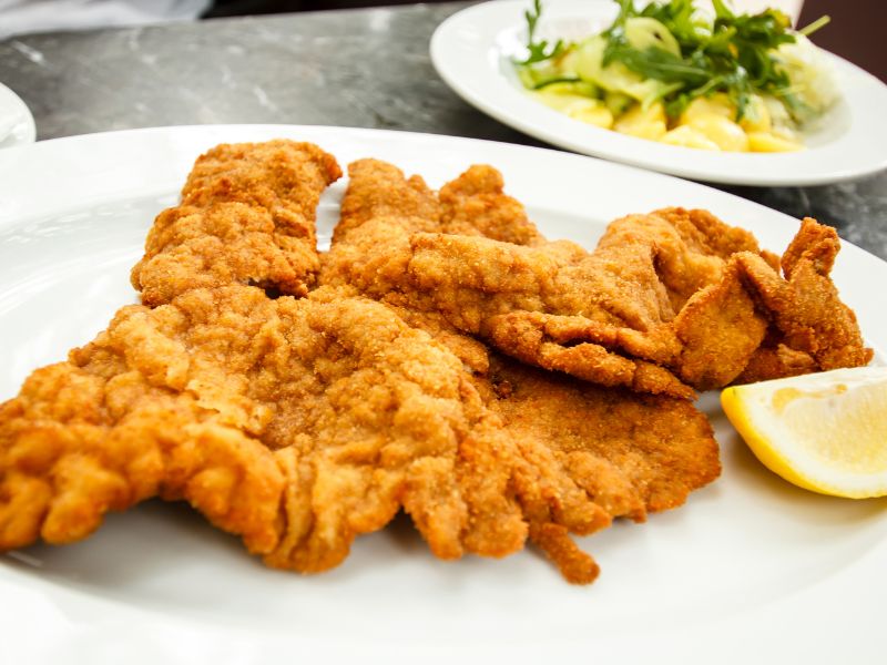 a plate of schnitzel with potato salad behind it