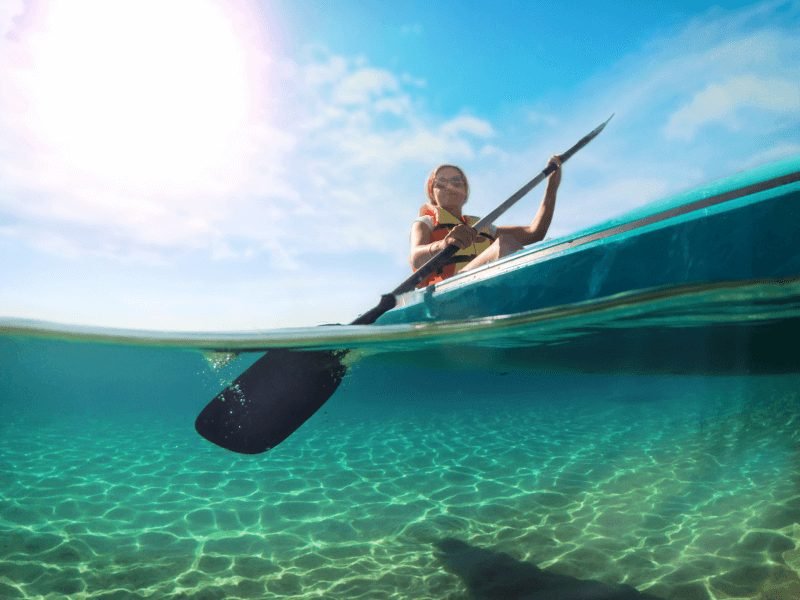 woman kayaking and smiling from a low angle photo with very clear water