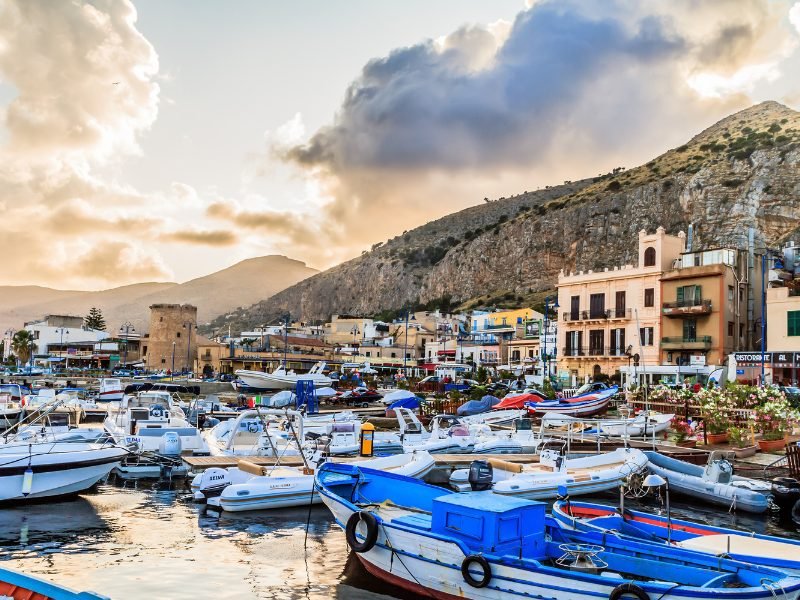 palermo harbor at sunset with boats and clouds and restaurants on the harborside