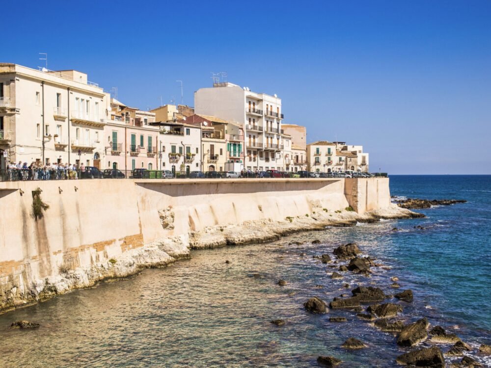 seawall and buildings on the edge of the ocean with people walking along the water's edge