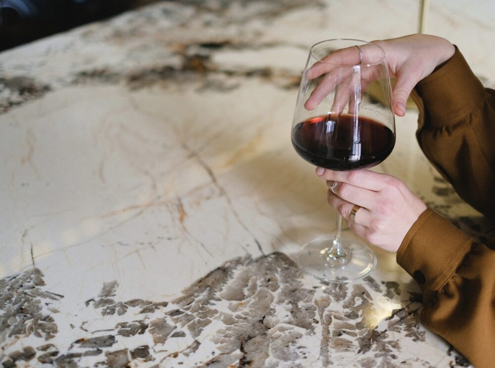 persons hand cradling a glass of red wine on a marble countertop