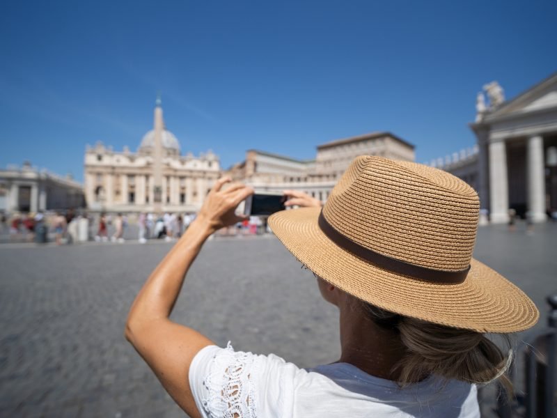 person with shoulders covered wearing a hat and taking photos of the vatican city