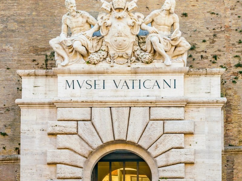 sign for the vatican museum with sculpture on a brick building