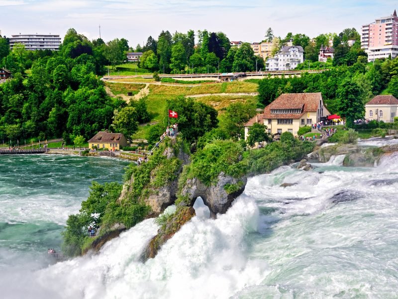 rhine falls - a large waterfall with a town in the background, one of the most beautiful places in switzerland