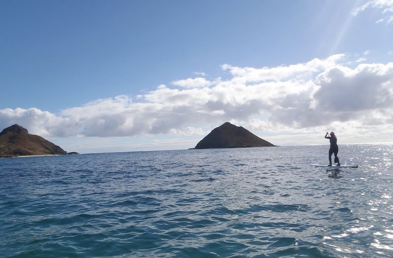 person paddleboarding in the ocean with two mokes (islands) in the distance on a sunny day in oahu