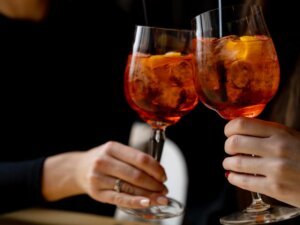 two hands clinking together an aperol spritz for aperitivo time at the end of the day in milan