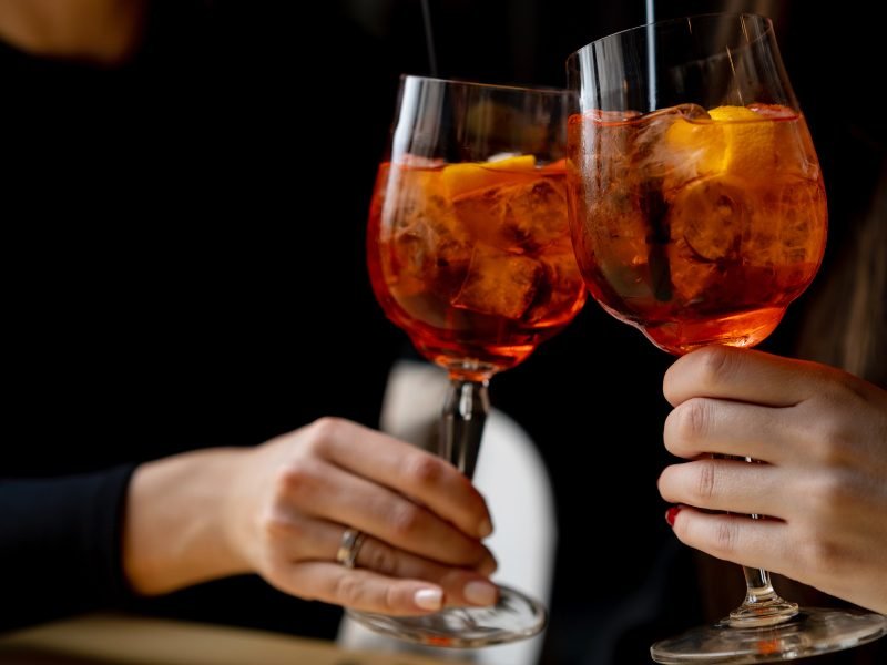 two hands holding aperol spritz and clinking glasses