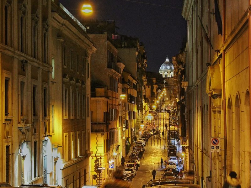 street scene down a main road in rome at night with lit up street