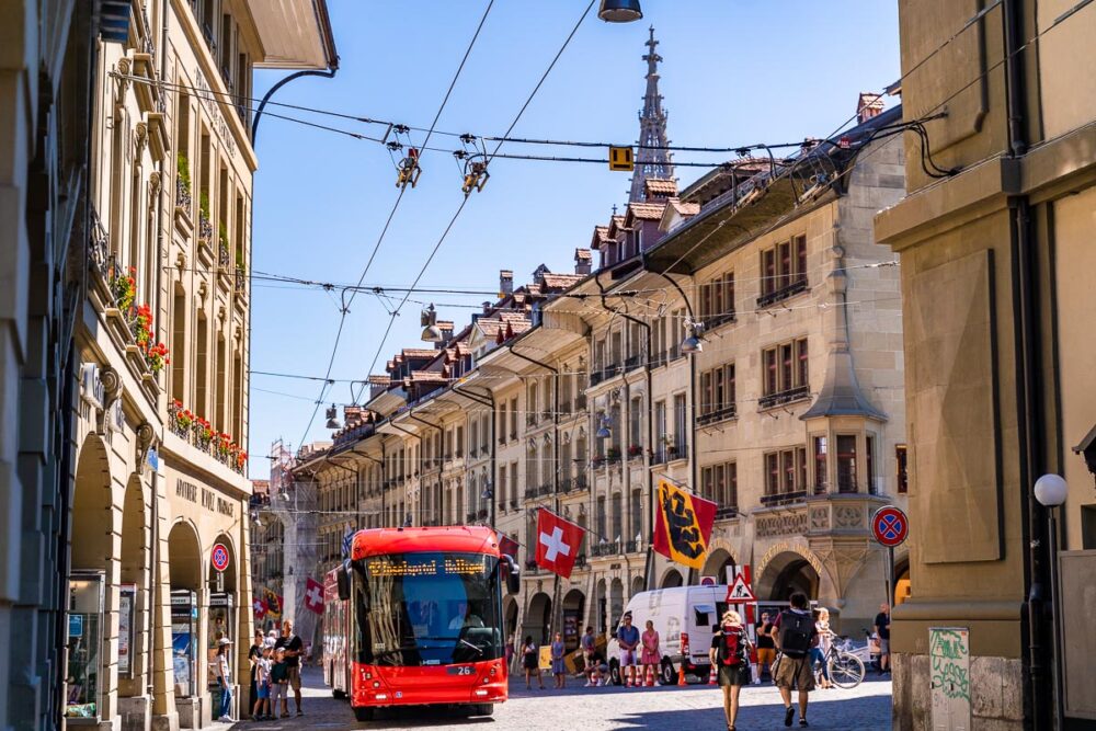 the old town of bern with a tram, swiss flags, and tourists visiting the beautiful town cneter