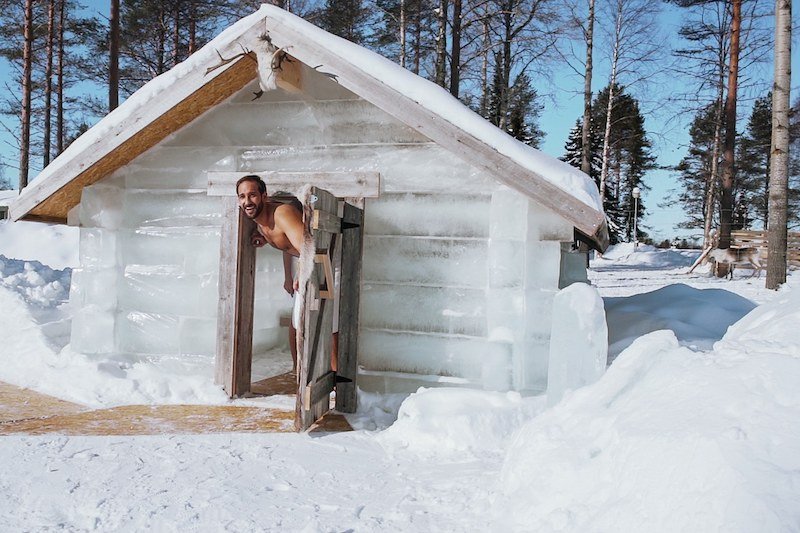 A man in a towel enjoying the ice sauna on the grounds of Apukka Resort during a winter day with forest and snow in the background.