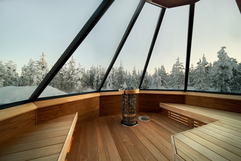 Glass ceiling on the sauna with wood benches and rocks to heat the sauna in the typical Finnish style. The glass windows allow you to see a winter landscape around you.