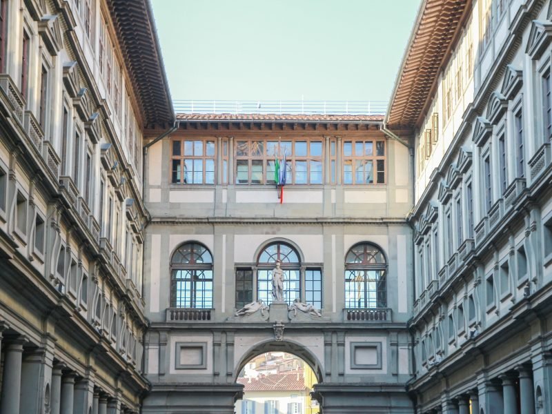 the uffizi gallery in florence with statues, flags, windows, detailing on architecture