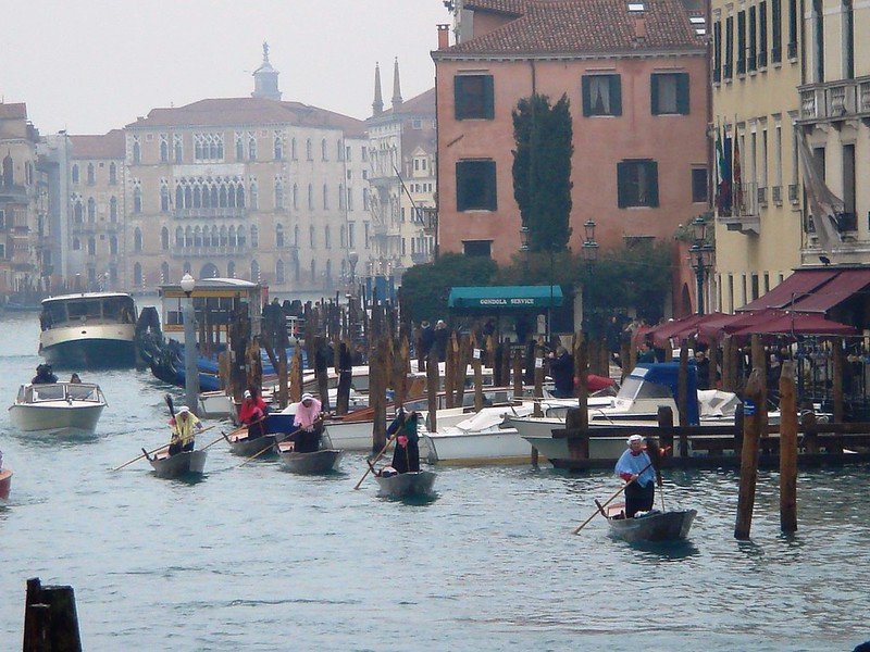 Men dressed up as witches rowing gondolas through the water on a foggy day in Venice in January