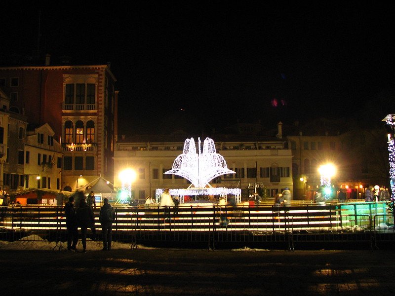 People ice skating in the dark with lit up displays in Campo San Polo in Venice, Italy on a winter night