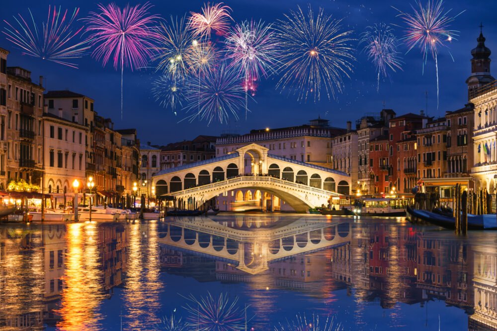 Fireworks colorful in the sky bursting over the bridge of Rialto which spans Venice's Grand Canal, you can see the reflection of the fireworks in the water below.
