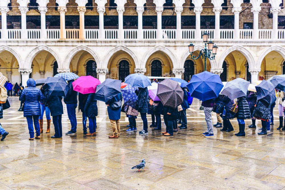 Tourists queuing up in St Marks Square in front of Doge's Palace wearing rain clothes and umbrellas in the rainy weather of Venice in winter