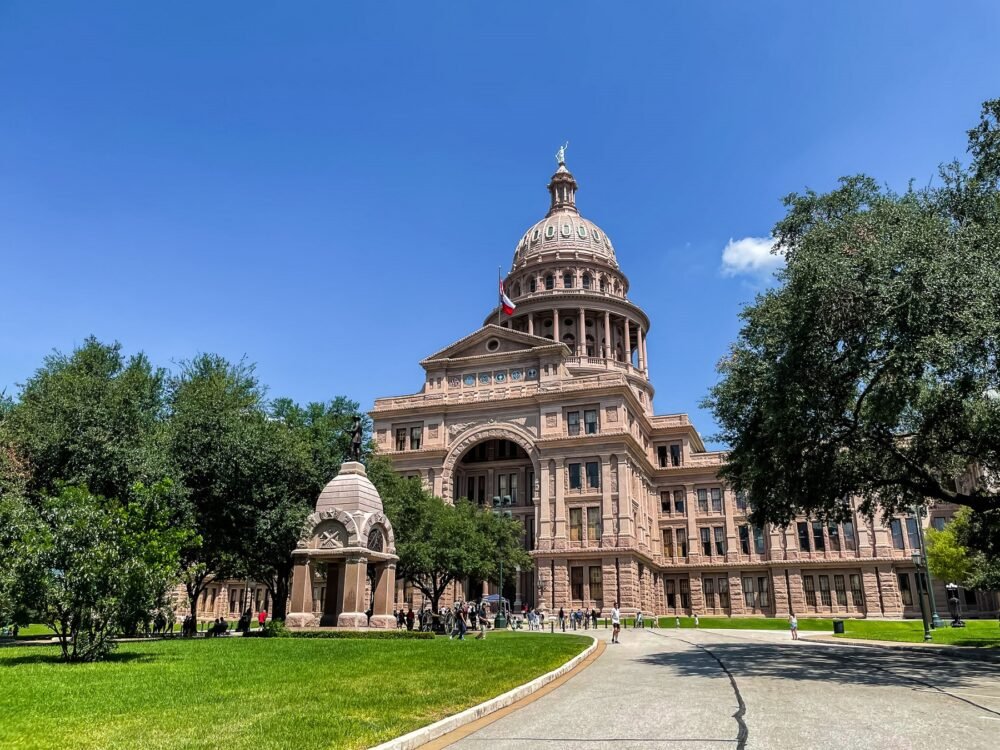 The brown building of the Texas Capitol Building in the heart of Austin surrounded by green spaces and trees.