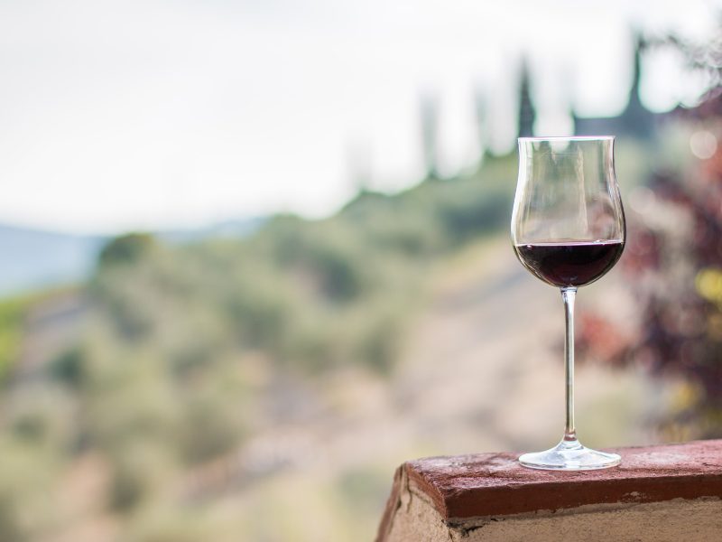 small taste of red wine standing on the table, blurry vineyard behind it