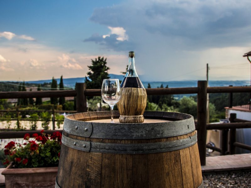 A bottle of Chianti on a barrel with an empty wine glass overlooking the rest of Tuscan countryside