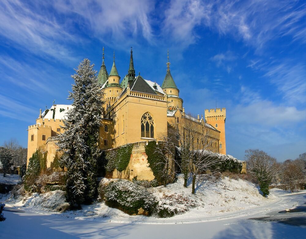 Snow-covered Bojnice Castle with beautiful snow on the landscaped elements and chateau-style architecture similar to what you'd see in France.