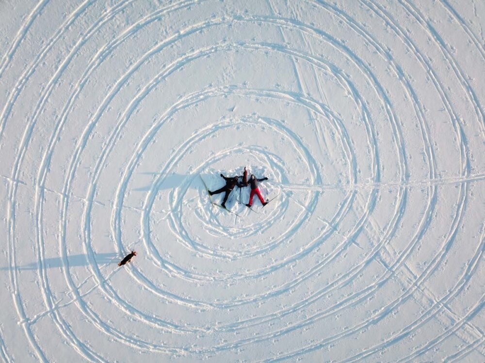 Aerial shot of two people laying down in the middle of circles drawn by ski tracks