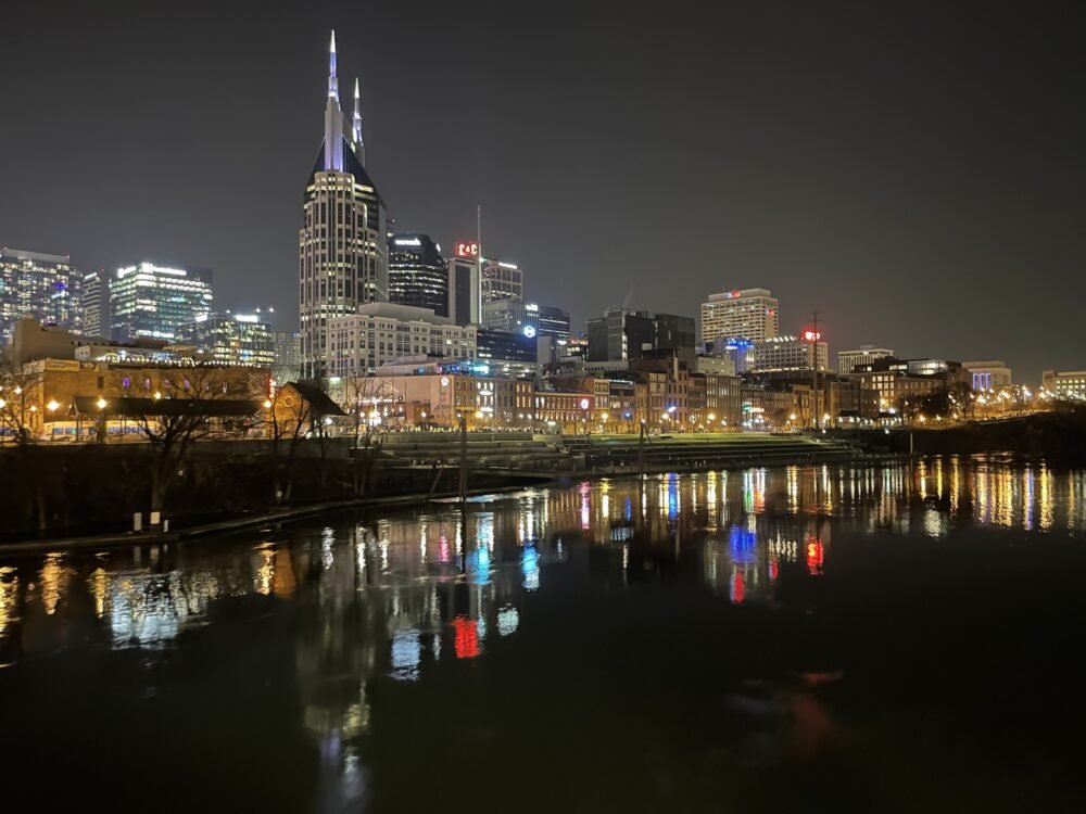 View of the Nashville skyline from the Cumberland river with the buildings all lit up and showing reflections in the dark water of the river