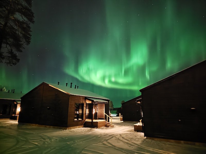 Log cabin style arctic chalets with the aurora in the night sky behind it.