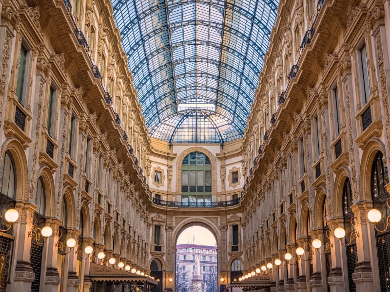 Lit up sconces leading the way to the main archway in the Galleria Vittorio Emanuele, with a beautiful glass and iron ceiling, that leads out onto a beautiful piazza in Milan.