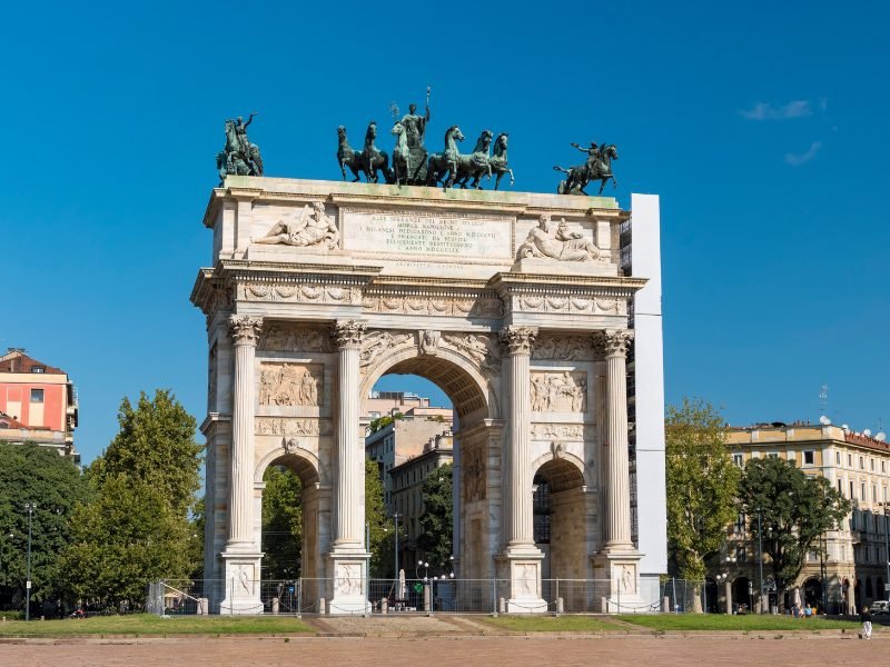 A classic European-style triumphal arch with four pillars, three archways (one larger and taller in the middle) and figures sculpture on the top of the arch.