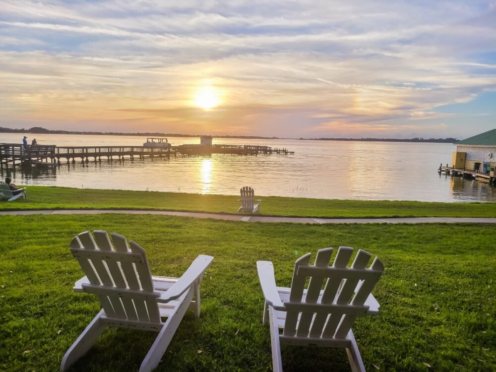 Two deck chairs on the lawn, looking out onto the lake at sunset, with beautiful pastel colors on the horizon