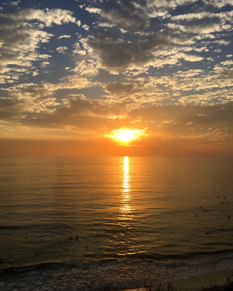 view of san diego at sunset with surfers enjoying a last surf before the sun sinks below the horizon. sky is orange and beautiful.