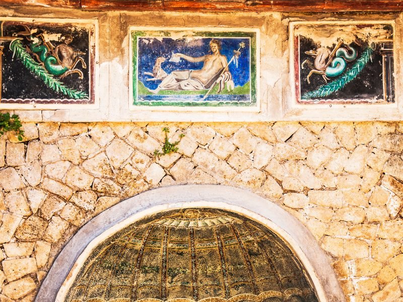 Three beautiful and vibrantly colorful Roman frescoes over a small niche in the wall, showing the detailed artwork that still remains preserved in Herculaneum over several thousand years since the eruption of Mount Vesuvius