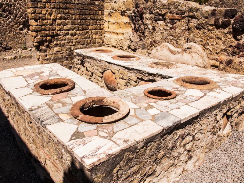 A portion of the archaeological site at Herculaneum in Italy, showing holes in the ground, perhaps used for drainage or sewage.
