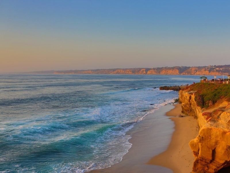 Sunset light falling on La Jolla Cove, with sand below and cliffs, and beautiful sunset colors