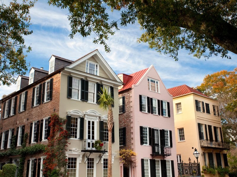 The rainbow row in Charleston with colorful facades and brick walls on the sides with trees above the houses